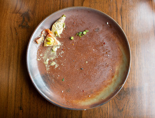 Empty dirty brown round plate with some leftover food on wooden table