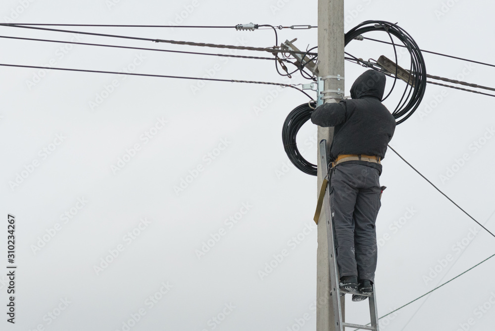 Wall mural electrician laying a new power line wires on a lamp post outdoors.