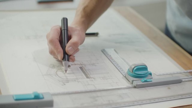 Engineer draws buildings on the table using a pencil and ruler. An architect creates a building design on paper using a marker and ruler