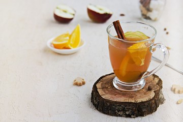 Apple cider with spices. Alcoholic or non-alcoholic hot drink made from fresh unfiltered apple juice with spices, apple slices and orange in a glass mug on a light concrete background. Copy space.
