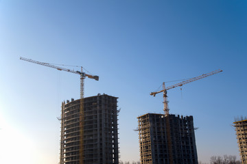 Tower cranes constructing a new residential building at a construction site against blue sky. Renovation program, development, concept of the buildings industry.