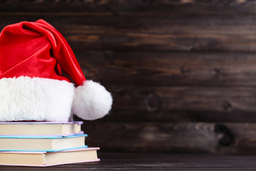 Red santa hat with stack of books on brown wooden background