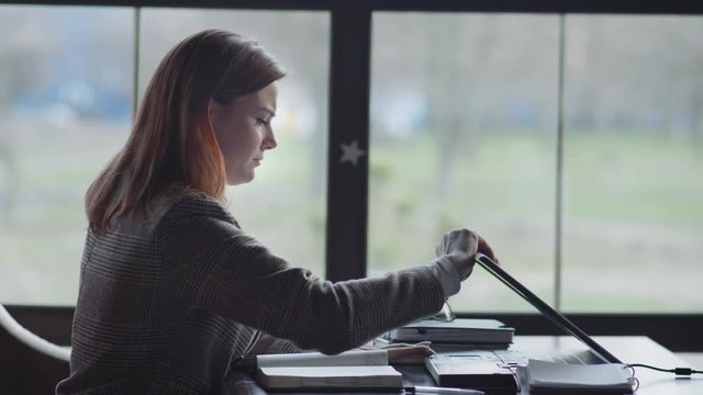 stress at work, a young tired businesswoman is nervous because of problems at work online, knocks on the table with anger and closes her laptop while sitting in coffee by window