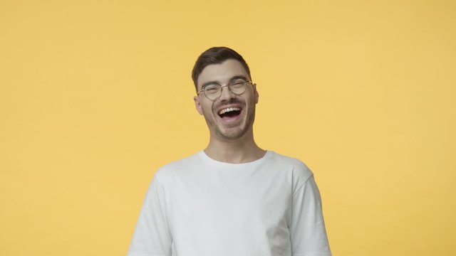 Attractive young man with bristle, wear glasses and white casual t-shirt, starts to laugh from hillarious joke, having friendly conversation, chuckling, watching comedy, stand-up, giggle and smile