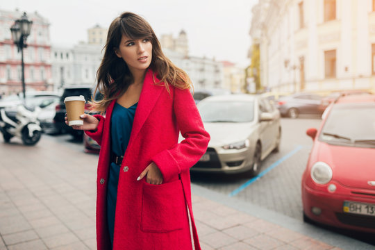 stylish woman in red coat walking in street with coffee