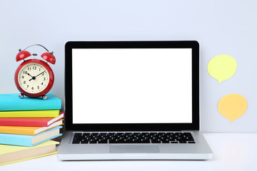Laptop computer with colorful books and red alarm clock on grey background