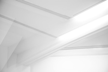 Ceiling and glowing girders with lamps. Abstract architecture fragment. Modern office building interior with triangular white concrete elements. Diagonal geometric composition in light gray halftones.