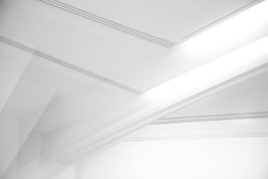 Ceiling and glowing girders with lamps. Abstract architecture fragment. Modern office building interior with triangular white concrete elements. Diagonal geometric composition in light gray halftones.