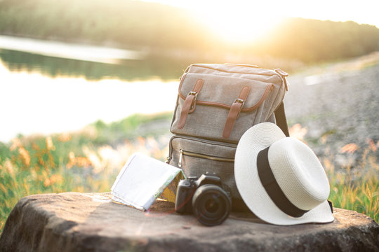 Travel with backpack, hat, map and camera at sunset.