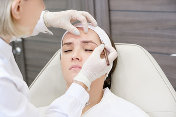 Microblading in beauty salon. Hands of an unidentified master make a preliminary drawing with a...