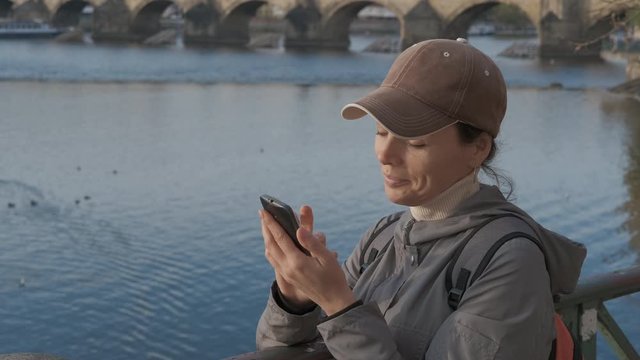 Rest by river in the city. Cute girl with a smartphone on the background of the old