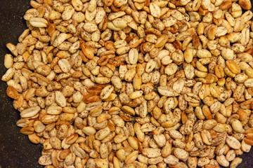 Roasted peanuts shades of yellow and brown, sprinkled with pepper appetizing appearance lies in the kitchen on a black pan.
