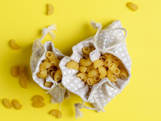 The dry macaroni is stuffed into cotton bags and laid out on a bright yellow background. Top view, can be used as background and creative pasta application