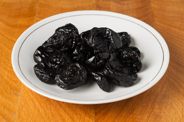 Dried black plum fruits (prunes) in a white plate on a wooden work