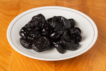 Dried black plum fruits (prunes) in a white plate on a wooden work