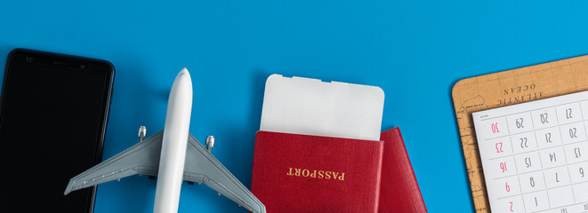 Topy airplane with passports, calendar, and mobile phone on blue background, flat lay.