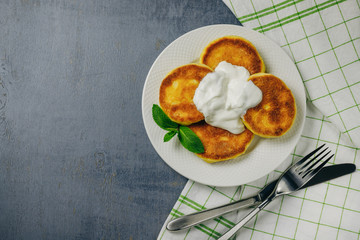 Pancakes with fresh mint and sour cream on white plate. Healthy breakfast food. Table top view. Grey background