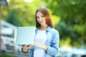 Fototapeta premium Young woman holding laptop computer on the street