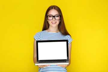 Young woman showing blank laptop screen on yellow background