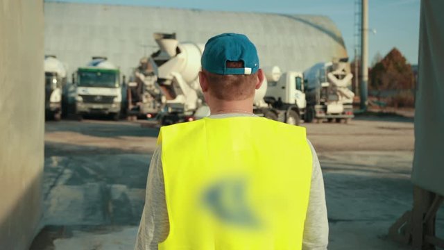 In picture, it can be observed that worker is watching the movement of truck. Worker is in charge of that, and he will instruct the truck driver.