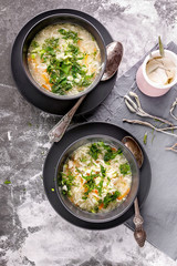 Chicken noodle soup with herbs and cheese sauce on a gray concrete background. Vertical shot. Top view