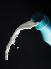 milk pouring from bottle or white liquid splash isolated on black background