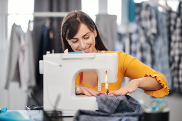 Focused charming caucasian fashion designer sitting in her studio and sewing beautiful evening dress.