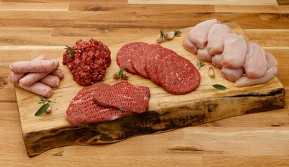 A platter of raw meat, inc beef, chicken and pork, with garlic and herbs on a wooden board, alternative.