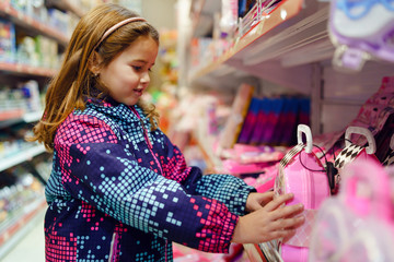 Fototapeta premium Small girl child looking at the toy picking present at the shelve of the shop ardor face