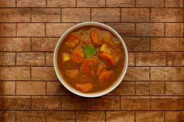 A bowl of delicious hearty winter vegetable soup, in a rustic bowl, on a checked wooden backgdrop.