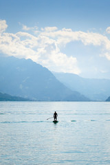 Obraz premium Silhouette of a man standing on a paddleboard on Lake Brienz in Switzerland. Mountains in the background. Active lifestyle, sports. Amazing background, lifestyle concept