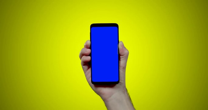 man's hand holding smartphone with blue croma key on yellow background swipes down one time 