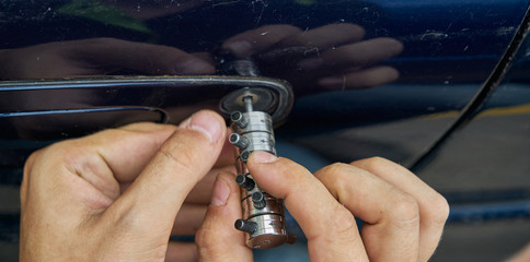 Locksmith opening with the lockpicker a blue car that its owner has lost the keys