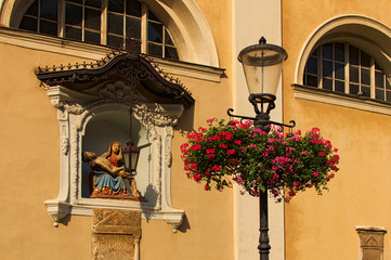 Fototapeta na wymiar Ljubljana, Slovenia-September 29, 2019: Medieval facade of St. Nicholas's Church at Cyril and Methodius Square. Decorated by Bible?s scene. Ancient lantern with flowers on the pot in the foreground