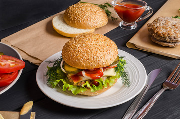 Ready-made hamburger with ingredients on a plate on a black wooden background. For advertising, menu.