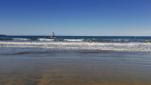 Wind surfing in El Medano, Tenerife, Canary Islands. 4K UHD footage of Atlantic ocean bay. Person on windboard rides on water along the shore during sunny day. Watersports, travel vacation concept