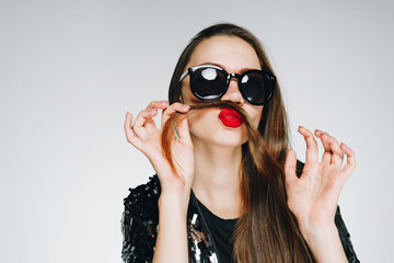 stylish girl playfully puts her hair to her face instead of a mustache. gray background