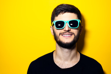 Studio portrait of young smiling man wearing sunglasses on yellow background.