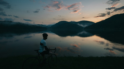 road bike driver looking to beautifull lake with clouds and reflection