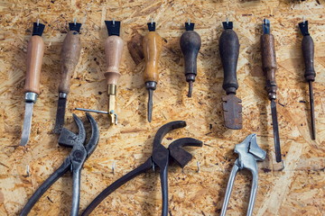 Group of old cobblers tools for handmade shoes production, awls and tongs for leather on wooden chipboard background, flat lay view