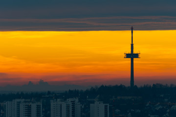 Television and radio broadcast tower on hill over the city of Regensburg with houses and skyscrapers during colorful winter sunrise