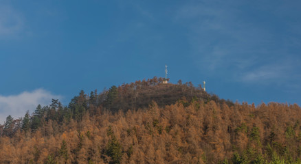 Hill over Perstejn village with blue sky and color forest