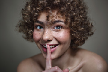 Vintage style portrait of smiling beautiful young freckled girl with keep quiet gesture, selective...