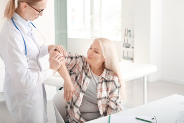 Doctor examining mature woman with joint pain in clinic