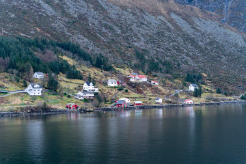 Fototapeta premium fishing village with colorful wooden fishing huts in the fjords of Norway on a sunny day in spring within a beautiful landscape shot from a boat 