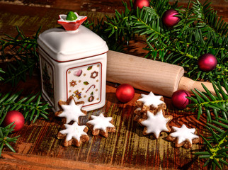 Christmas scene with cinnamon stars, rolling pin, a ceramic biscuit tin and other christmas decoration on an old wooden table.