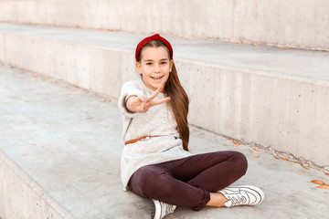 Cute fashionable girl showing victory gesture outdoors