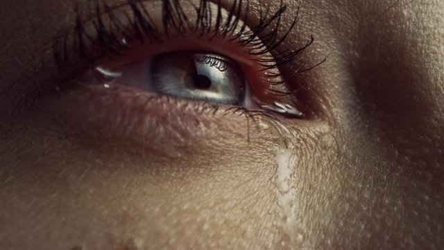 Close Up Macro Zoom Shot of a Crying Eye. Young Beatiful Female with Natural Light Blue, Yellow and Brown Color Pigmentation on the Iris. Mascara is Applied to Eyelashes. Tears are Flowing Down.