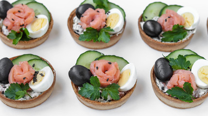 Holiday tartlets with cheese, salmon, black olives, quail eggs and cucumbers on white background, horizontal orientation
