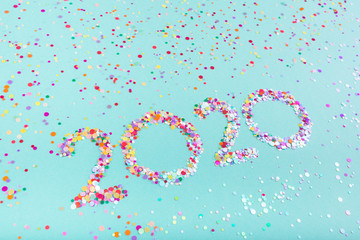 Creative number 2020 written in multicolored glitter on a mint color background. Copy space for text. Top view, flat lay. Holiday backdrop. New Year 2020 concept.